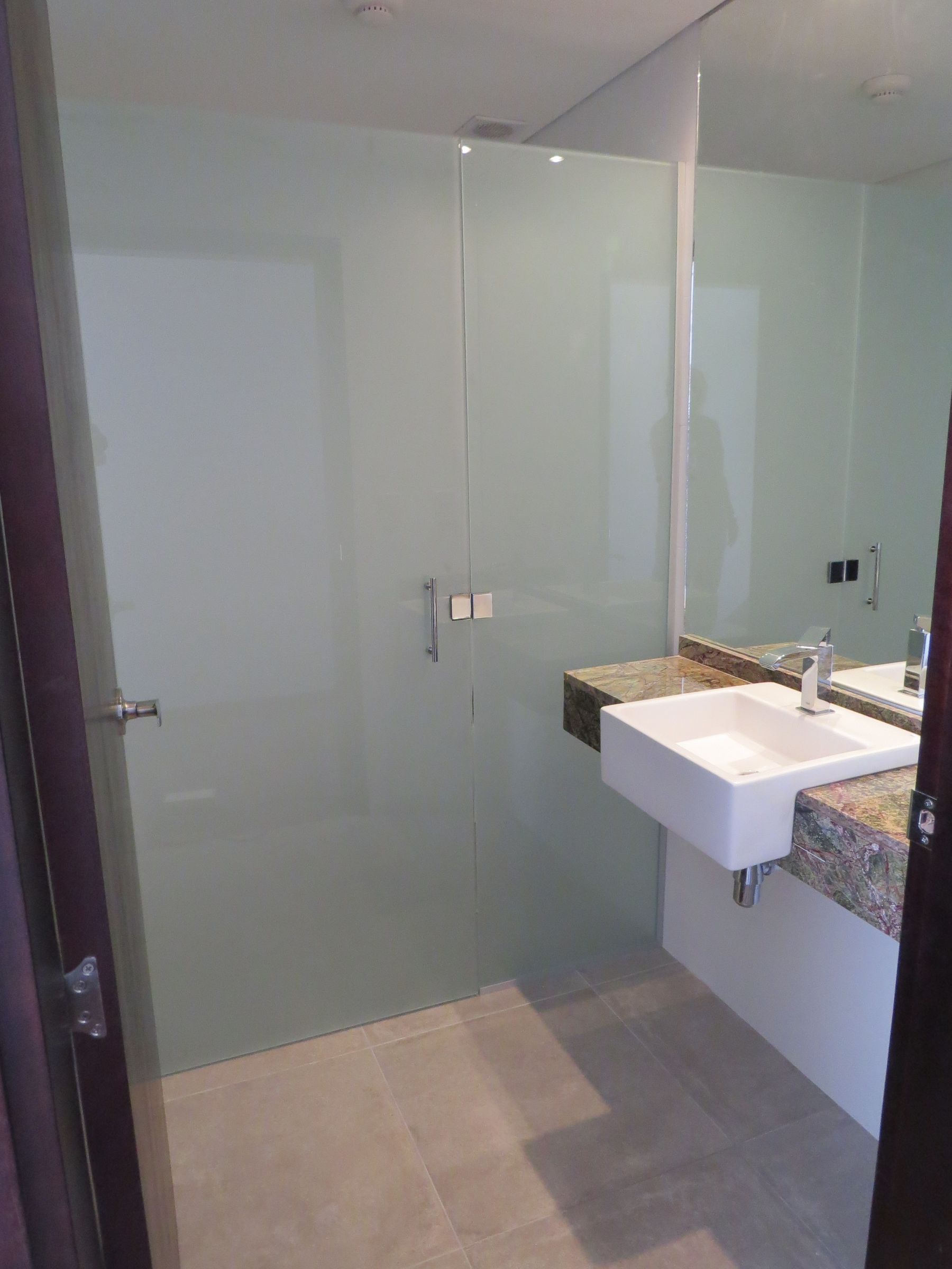 En la fotografía se aprecia un baño con pileta empotrada en una mesada de granito. Piso revestido en porcelanato y mampara de vidrio ahumado.